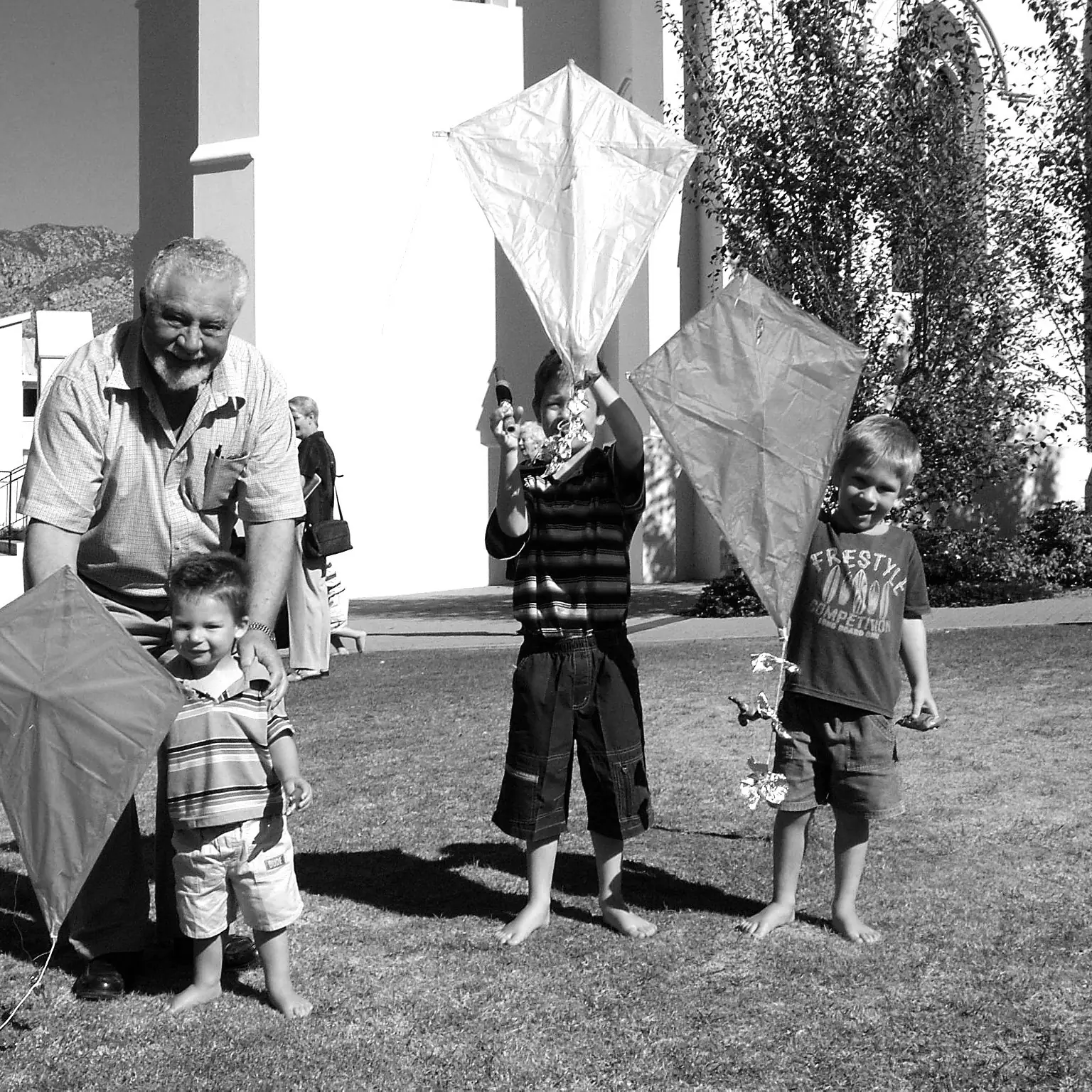 Three young boys holding kites on a lawn, with their grandfather crouched beside them